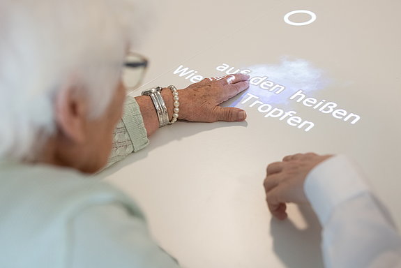 Eine ältere Dame beugt sich über einen Tisch, auf den Wörter projiziert werden.